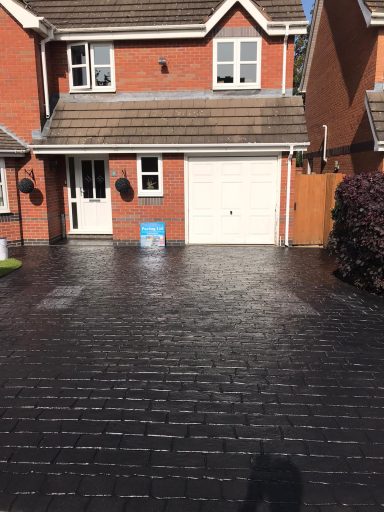 A brick driveway in front of a two-storey brick house with a garage.
