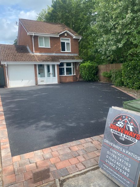 Tarmac Driveways Driveway in front of a brick house with a large paved area and greenery surrounding it.