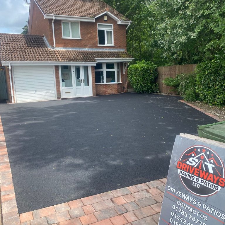 A well-maintained house with a newly paved driveway and greenery surrounding it.