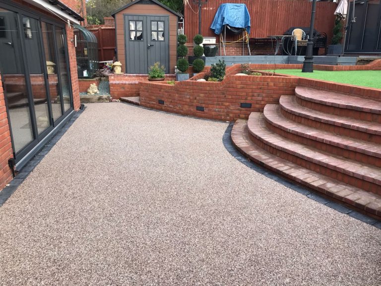 Paved garden area featuring steps, a wall, and garden structures in the background.