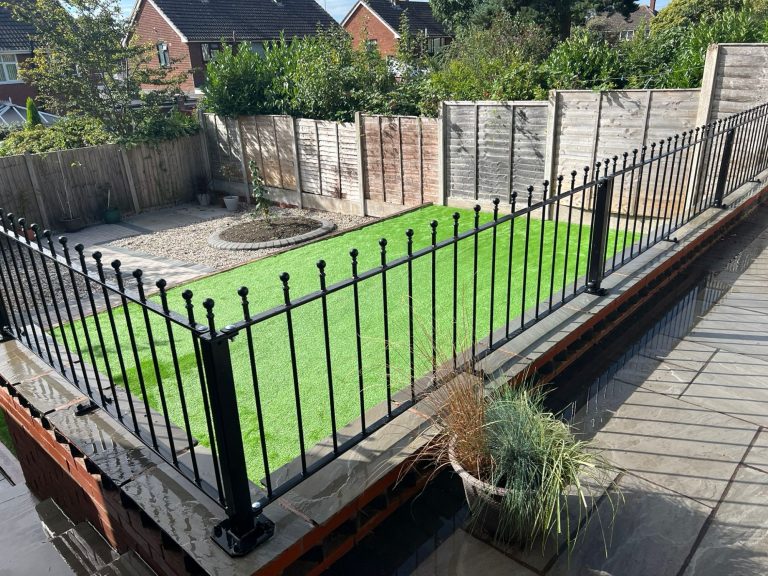 A fenced garden area with green grass and wooden fences, surrounded by houses.