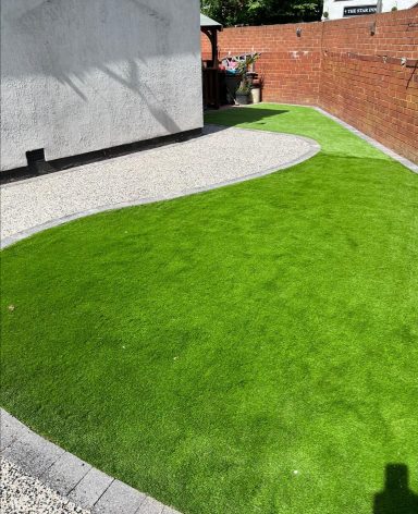 Lush green lawn with a curved edge and gravel pathway in a garden setting.