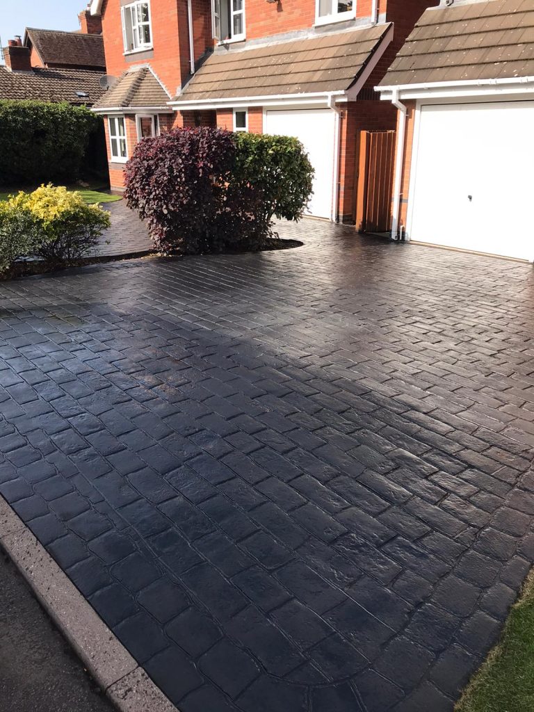 A well-maintained driveway with patterned paving and neatly trimmed plants.