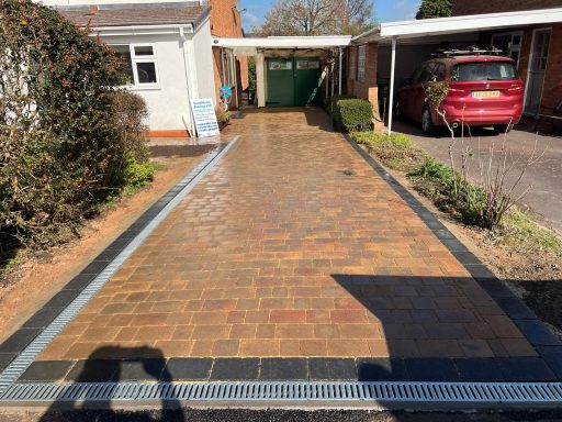 Paved driveway with a car parked in the distance and greenery along the sides.