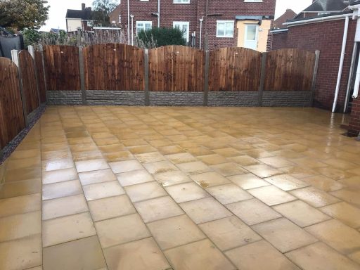 Paved outdoor area with stone tiles and wooden fencing in the background.