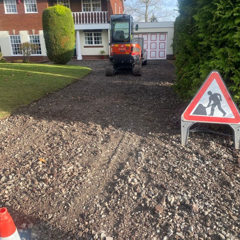 Small digger on a gravel driveway with a construction sign nearby.