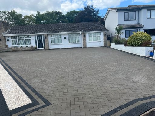 Bungalow with a paved driveway surrounded by neatly maintained gardens.