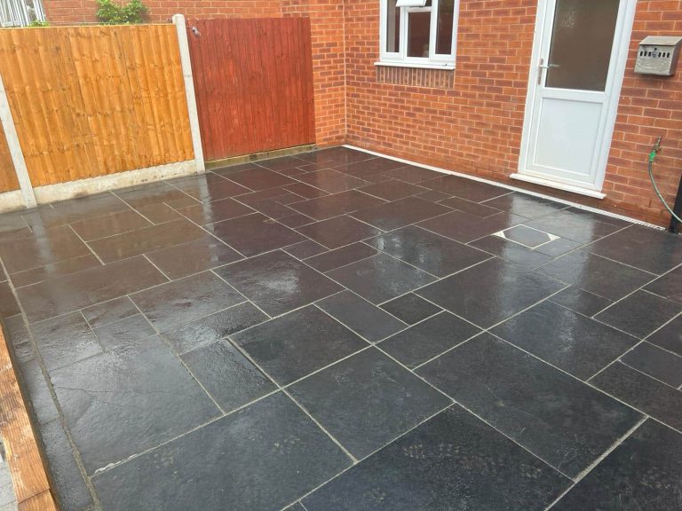 Paved outdoor area with black tiles, wooden fence, and a white door.