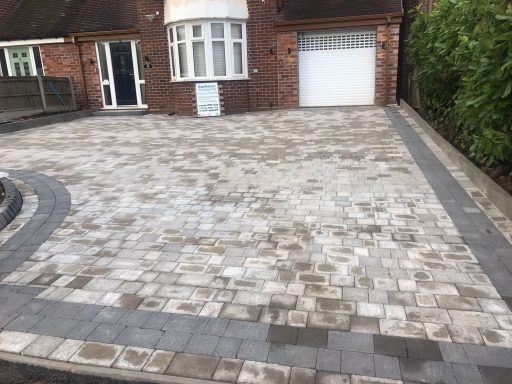 Paved driveway with light and dark grey stones beside a brick house.