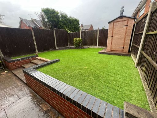 A small garden with artificial grass, surrounded by wooden fences and a shed.