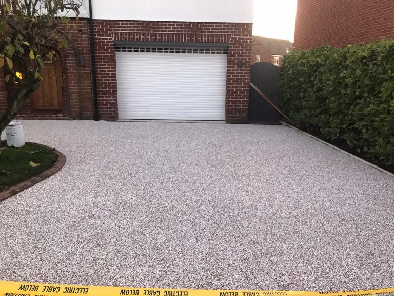 Gravel driveway leading to a garage, bordered by greenery and caution tape.