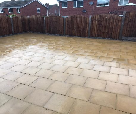 Patio area with clean, even paving stones, surrounded by wooden fencing.