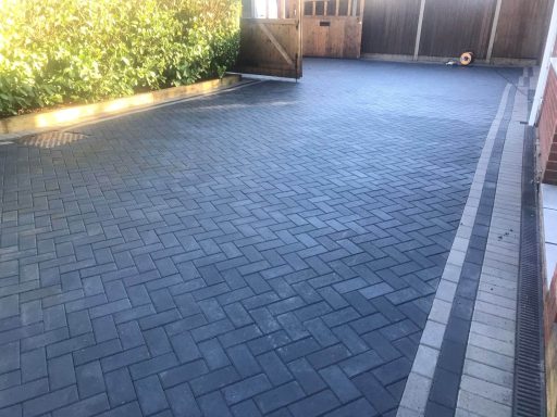 Paved driveway with a herringbone pattern and wooden gate in the background.