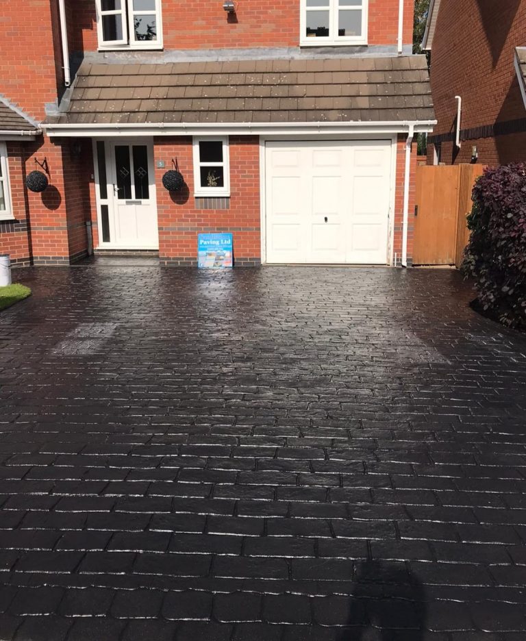 A tidy driveway in front of a brick house, with a garage and potted plants.