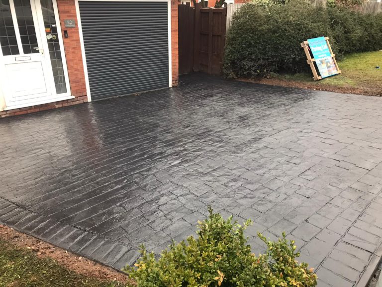 A freshly laid black patterned driveway next to a garage and a small bush.