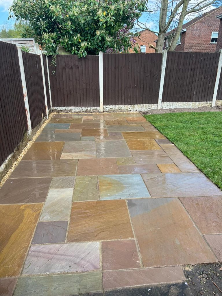 Paved garden area with sandstone tiles, neatly arranged, and green grass nearby.
