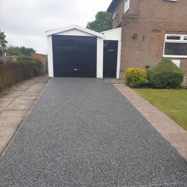 Driveway leading to a garage, with neatly trimmed hedges and a house beside it.