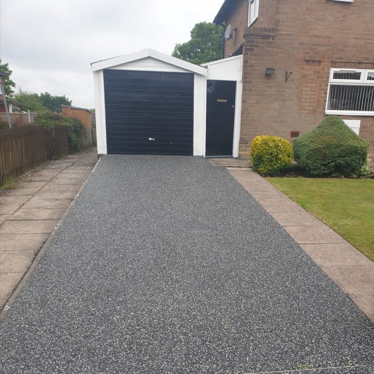 Driveway leading to a black garage, with a lawn and hedge on the side.