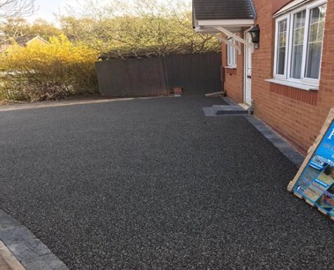 Newly laid dark gravel driveway beside a brick house, with a sign nearby.
