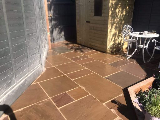 Paved outdoor area with a yellow shed and a small table and chairs.