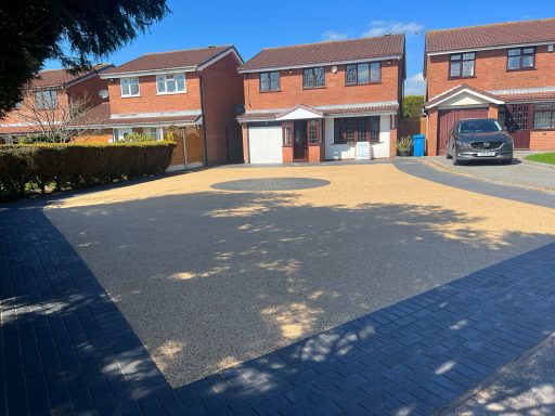 A driveway with a circular design and two houses in the background under a clear blue sky.
