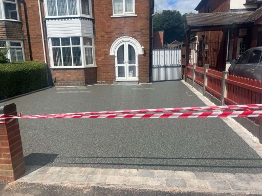 Freshly laid grey driveway with a barrier tape in front of a residential property.