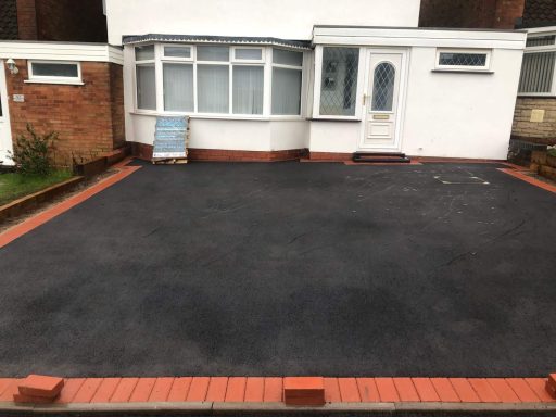 A freshly paved driveway with red brick edging and a small sign near the house.