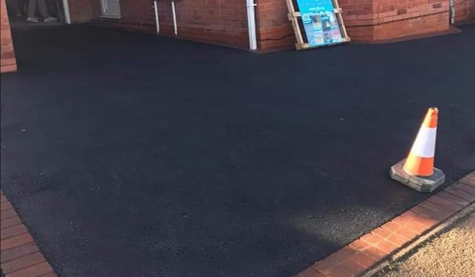 Freshly laid asphalt surface with a traffic cone positioned on the edge.