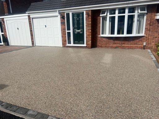 Driveway with a textured surface, adjacent to a brick house and two garage doors.