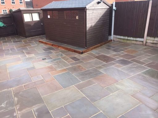 Paved outdoor area with a wooden shed and surrounding fencing.